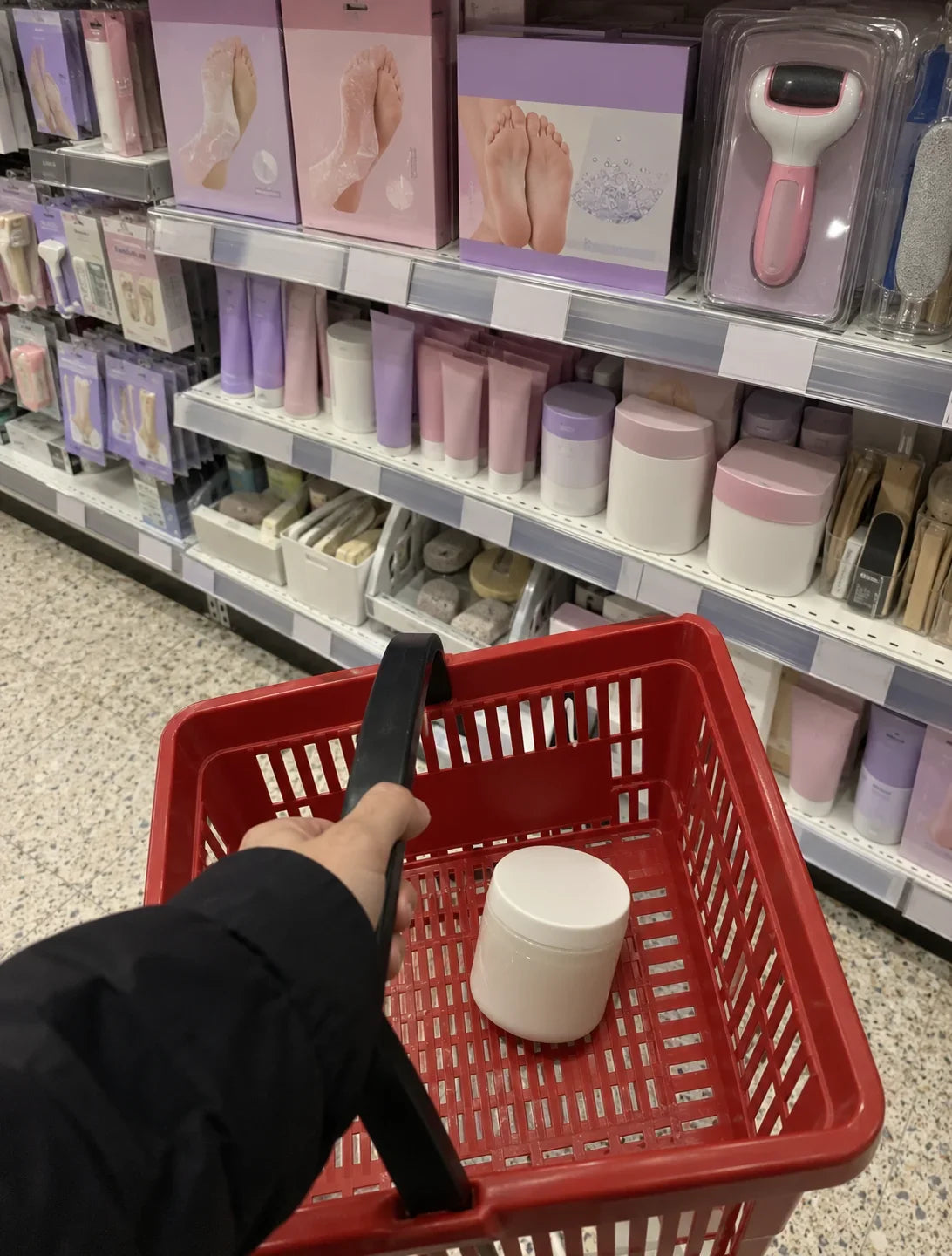 A basket in a chemist aisle of pastel foot care packaging, one jar of petroleum jelly in it