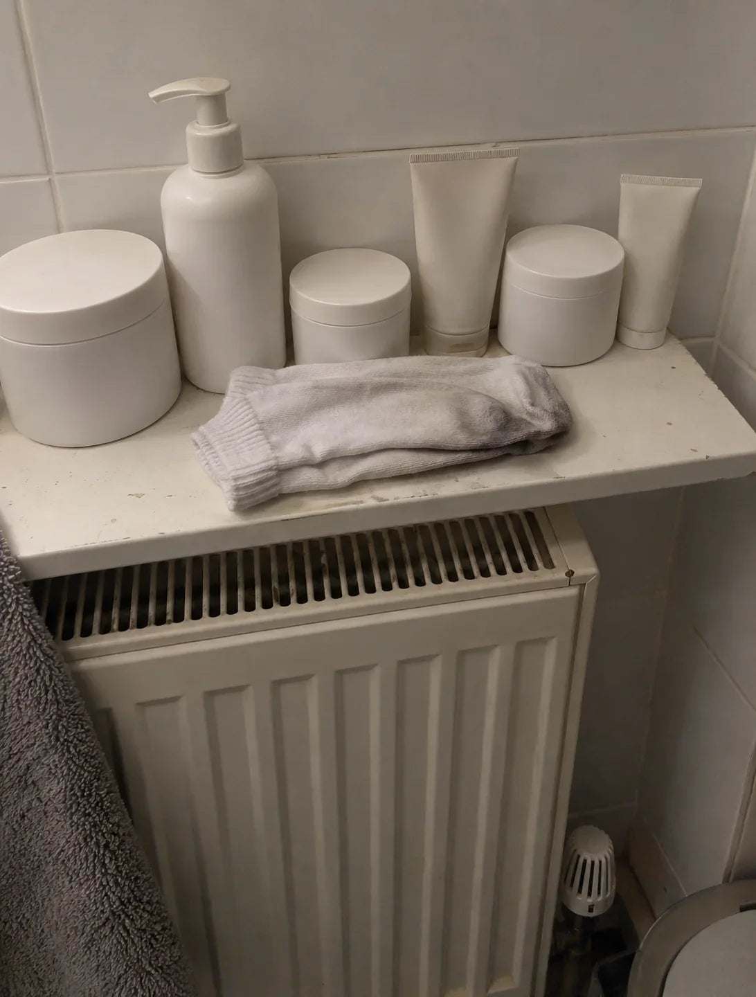 A bathroom shelf lined with emollient tubs and tubes, a pair of stiff cotton socks folded in front