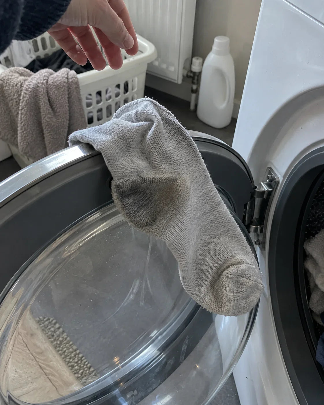 A thin cotton bed sock, inside out, hanging on the open door of a washing machine with a grey patch at the heel