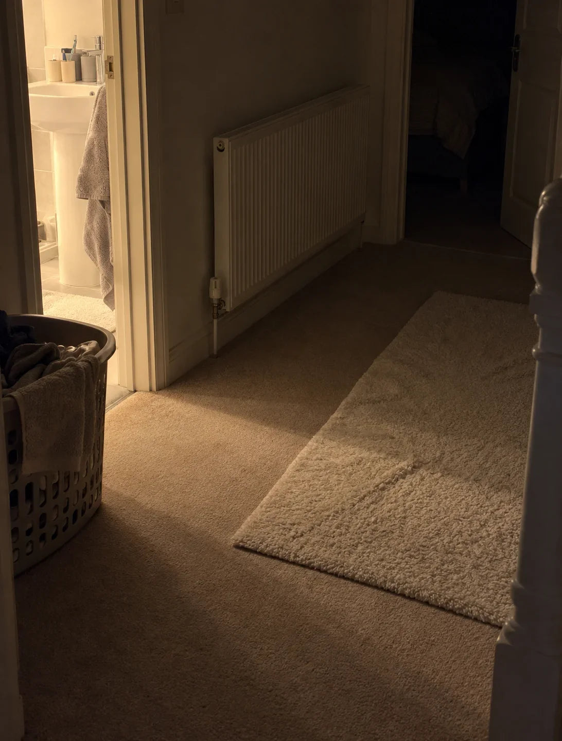 A landing at night, the bathroom light on at one end and the bedroom dark at the other