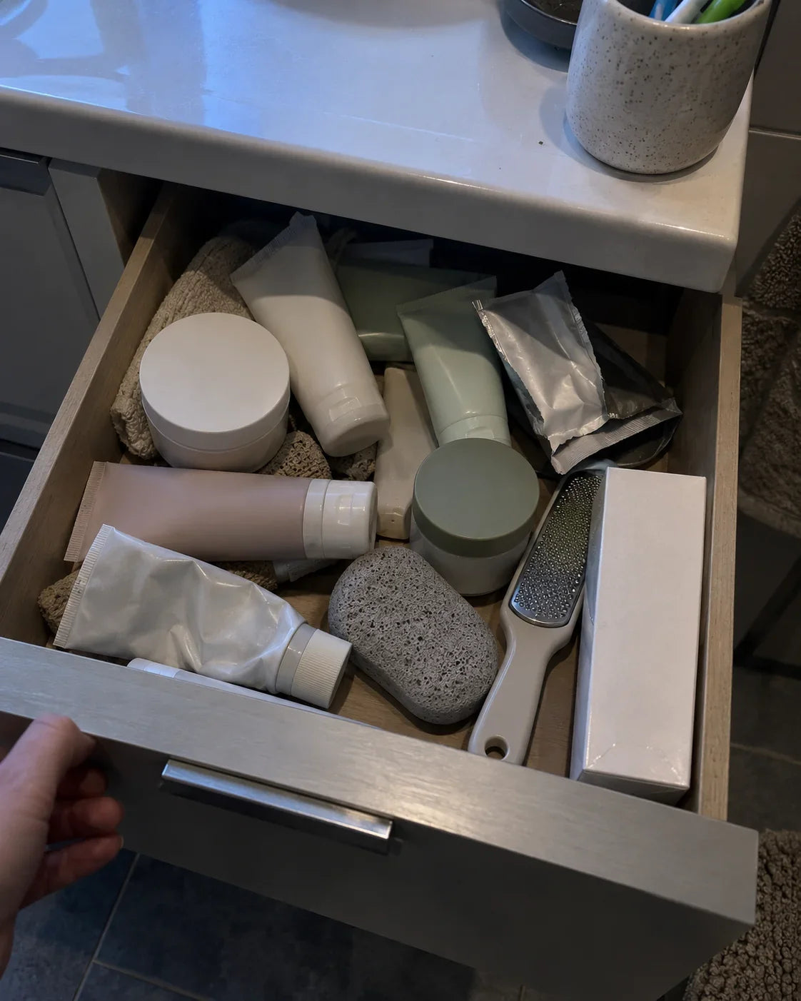 A bathroom drawer pulled open, full of half used foot creams, a pumice stone and a metal file